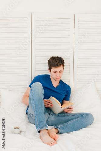 Man reading a book sitting on the bed