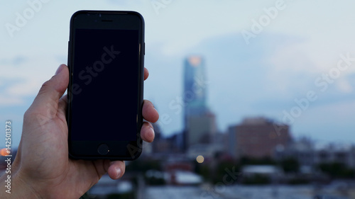 Holding iPhone in Hand in with downtown city in the background, authentic cell phone with modern style