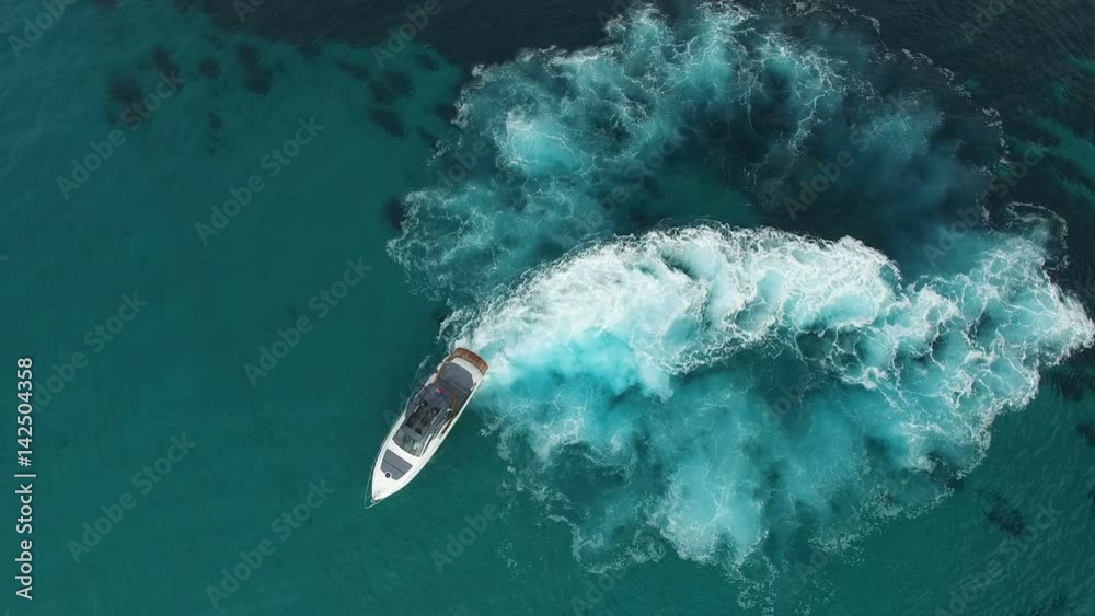 Perpendicular aerial view of a luxury yacht slowly navigating in clear blue waters.