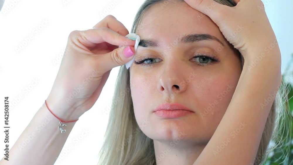 Cosmetologist washes away paint from eyebrows a cotton disk. End of the procedure. Cosmetologist washes away paint from eyebrows a cotton disk. End of the procedure.