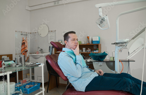 A man is sitting in an armchair by a dentist