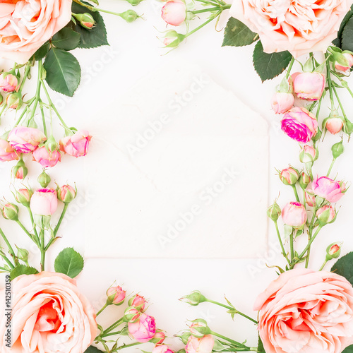 Floral round frame made of pink roses and paper envelope on white background. Flat lay, top view. Flowers background.