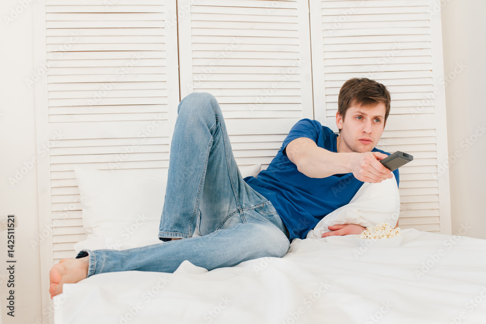 Man watching TV sitting on the bed eating popcorn Man watching TV sitting on the bed eating popcorn
