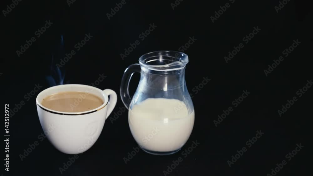 white Cup of coffee and a jug of milk on black background. white Cup of coffee and a jug of milk on black background.