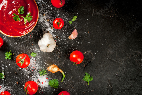 Fresh homemade organic tomato sauce or ketchup, in a small bowl. With the ingredients - parsley, onions, garlic, tomatoes, salt, pepper. On a black stone concrete table. top view copy space