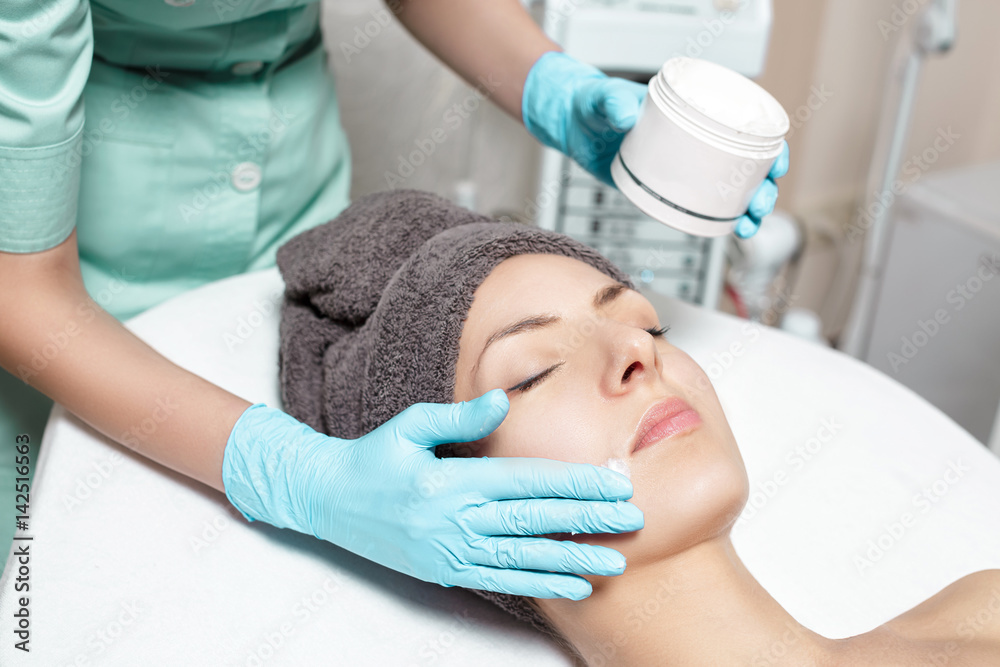beautician applies face cream on beautiful young woman in Spa salon. cosmetic procedure skin care. 
