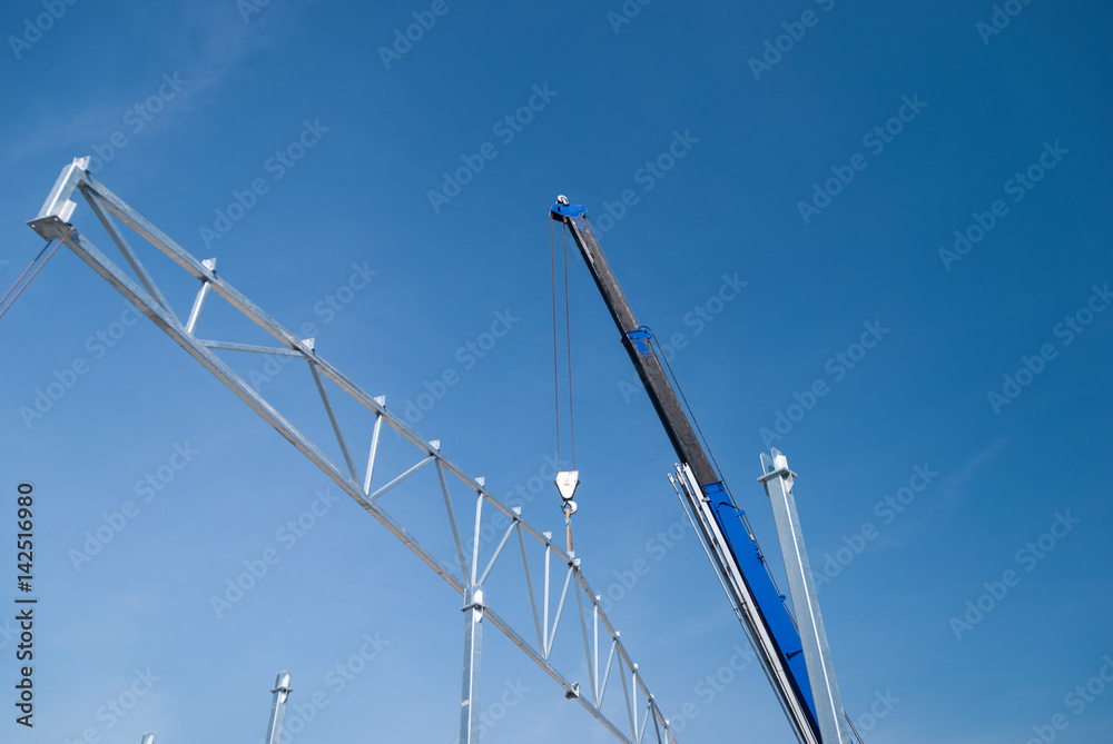 Crane lifting galvanized steel roof truss construction frames with deep blue sky in the background Crane lifting galvanized steel roof truss construction frames with deep blue sky in the background