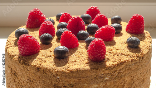 Honey cake decorated with raspberries and blueberries.