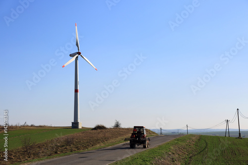 Turbina wiatrowa, wiatrak, ciągnik rolniczy na drodze.