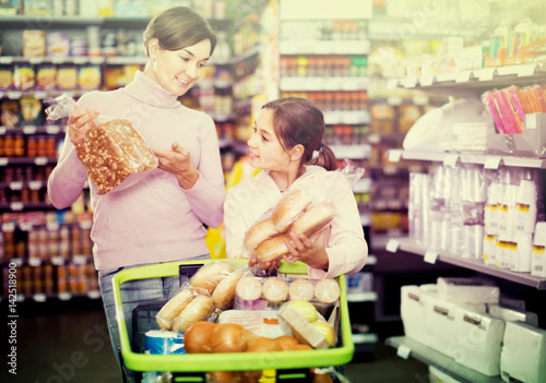 smiling woman with daughter choosing bread in supermarket