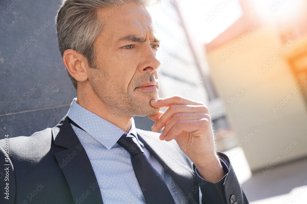Portrait of businessman waiting outside building, leant on wall Portrait of businessman waiting outside building, leant on wall