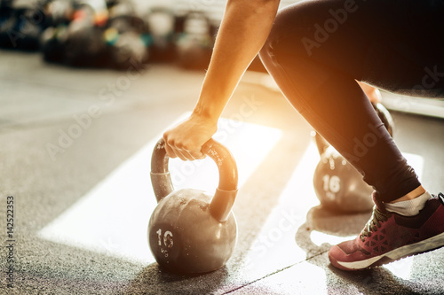 Muscular woman holding old and rusty kettle bell on to the gym floor. Focus on the kettle bell. photo