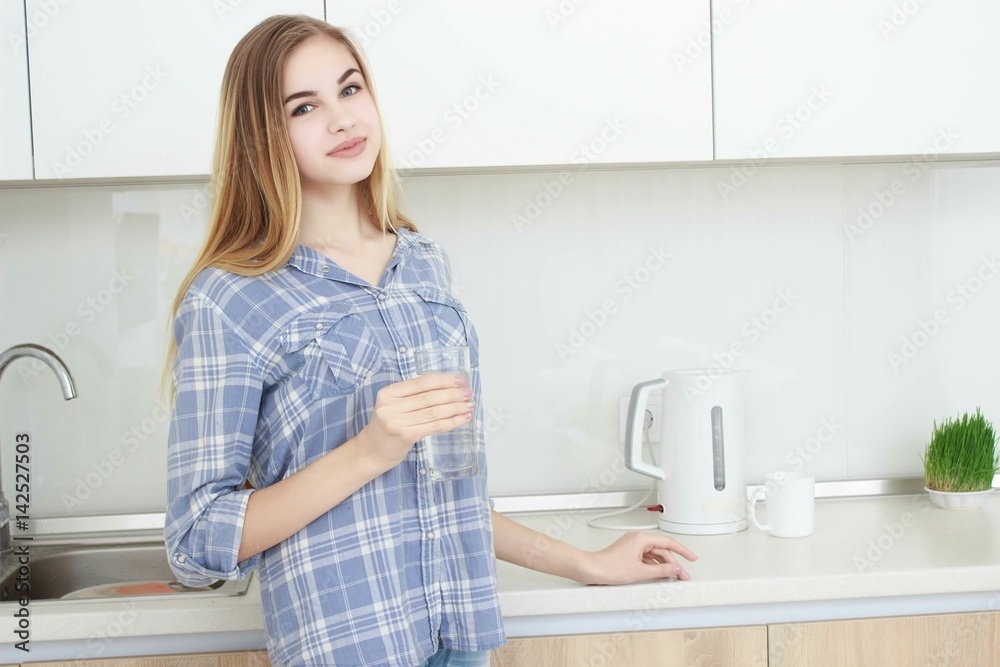 Beautiful young woman holds a glass with water on kitchen.
