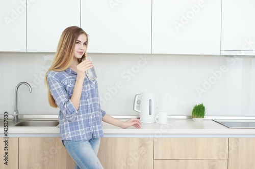 Beautiful young woman holds a glass with water on kitchen.