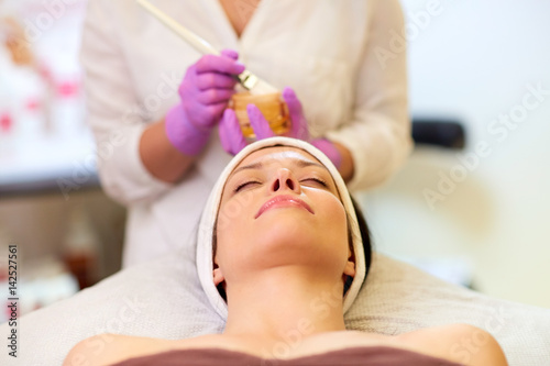 beautician applying facial mask to woman at spa