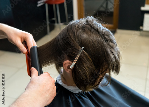 Male hairdresser is preparing for haircut of Beautiful woman in the beauty salon. He straightens hair.