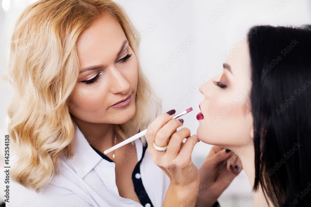 Make-up artist applying bright base color eyeshadow on model's eye and holding a shell with eyeshadow on background, close up Make-up artist applying bright base color eyeshadow on model's eye and holding a shell with eyeshadow on background, close up