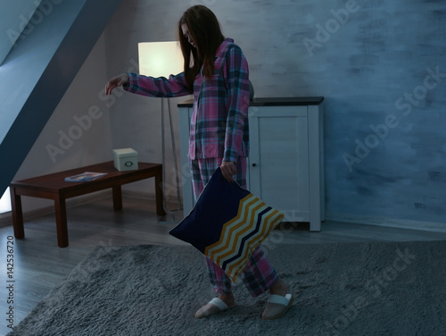Young sleepy woman with pillow suffering from somnambulism at home photo