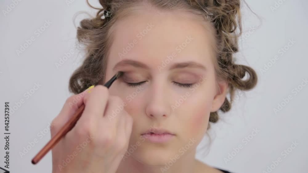 Professional make-up artist applies eye shadow to eyelid of model in white room. Beauty, makeup and fashion concept Professional make-up artist applies eye shadow to eyelid of model in white room. Beauty, makeup and fashion concept