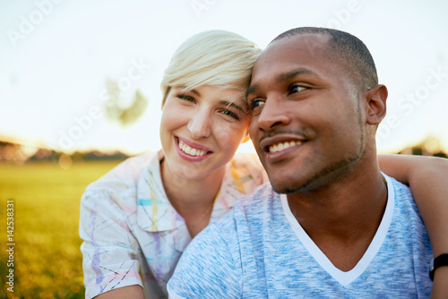 Mixed race couple of millennial in a grass field embracing for a fun tender moment