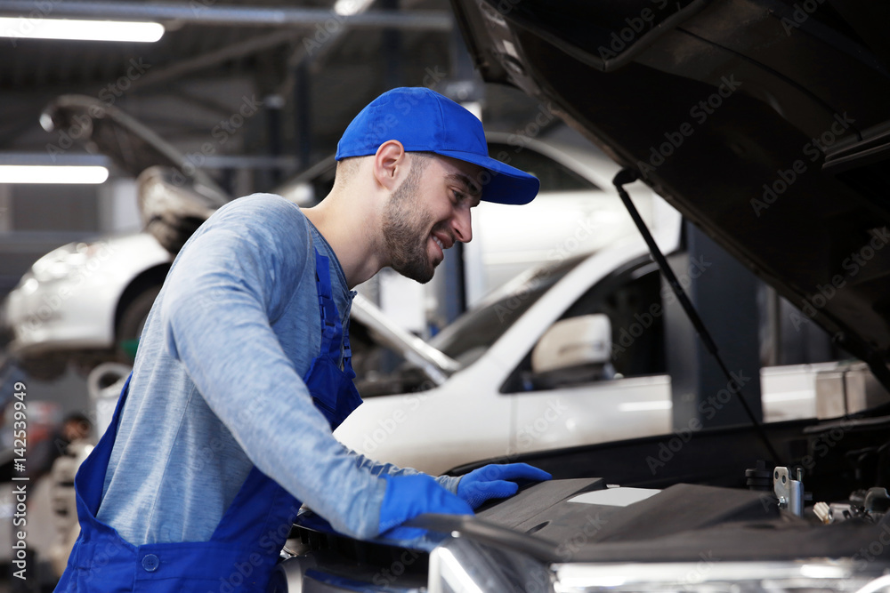 Young mechanic standing in front of open car hood Young mechanic standing in front of open car hood