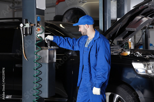 Young mechanic standing near auto lift in car service
