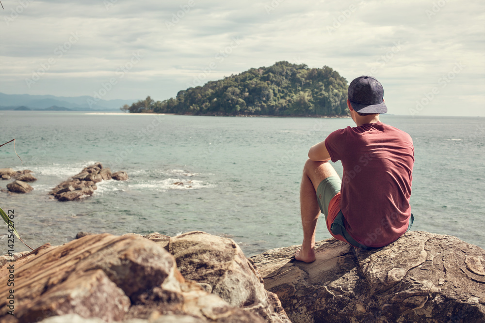 Mann auf Felsen schaut zur Insel hinaus Mann auf Felsen schaut zur Insel hinaus