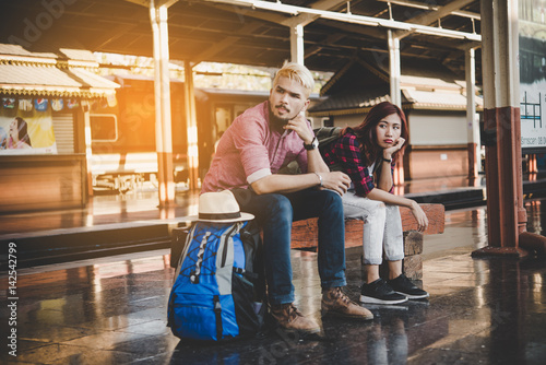 Young attractive hipster couple sitting and waiting for the train to go traveling. Travel concept.