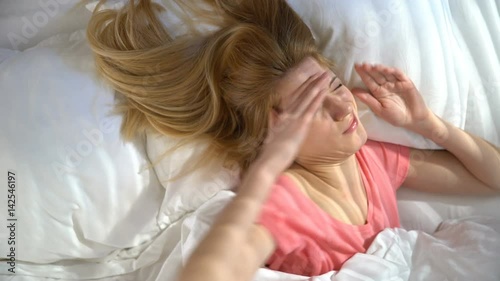 Unhappy sleepy young woman does not want to wake up in the morning and hiding under the blanket. Top view.