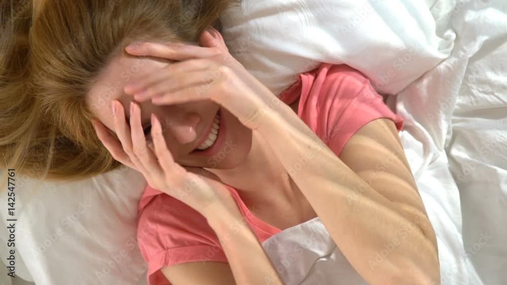 Young shy woman in bed smiling looking at the camera. Slow motion. Top view