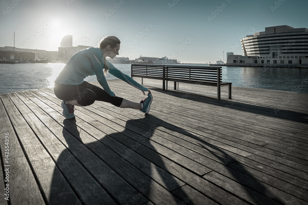 Woman do exercise after running on the wooden pier under sunligh