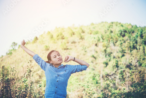 Young woman standing looking to a sky with raised hands while during hike in the mountain.