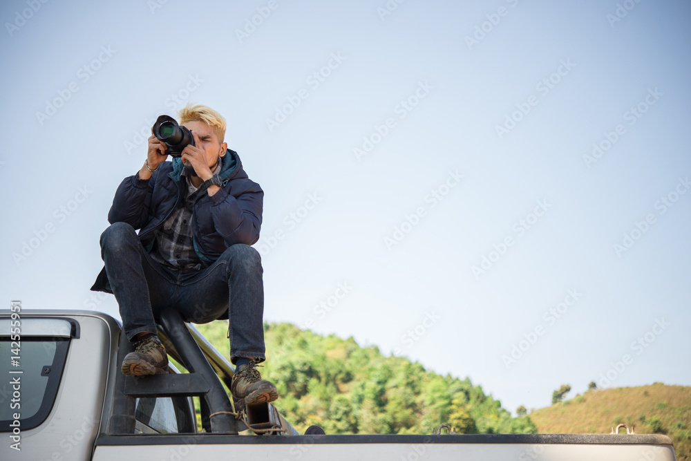 Young photographer sitting on his pickup truck photographing in mountain.