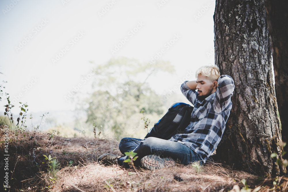 Portrait of young beard man sitting alone by a tree with backpack looking away enjoy with nature. Portrait of young beard man sitting alone by a tree with backpack looking away enjoy with nature.