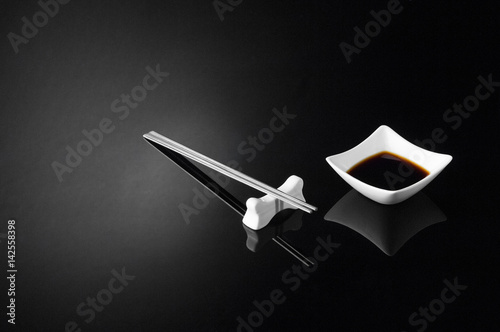 japanese sushi sticks and sauce pot with soy on a black background. metal chopsticks and sauce on a dark background