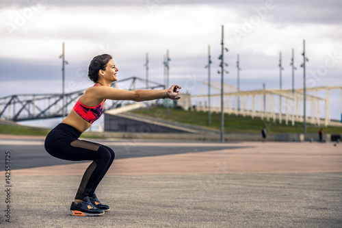 Young and attractive woman in sportswear is making squats in urban park  Barcelona  Spain. Minimalism concept.