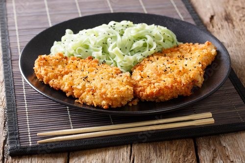 Chicken cutlet in breadcrumbs and green noodles with sesame close-up. horizontal