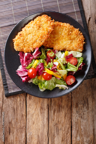 Chicken steak in breading Panko and fresh salad close-up on the table. vertical top view