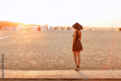 Junge schlanke Frau steht am Strand und schaut auf den Sonnenaufgang photo
