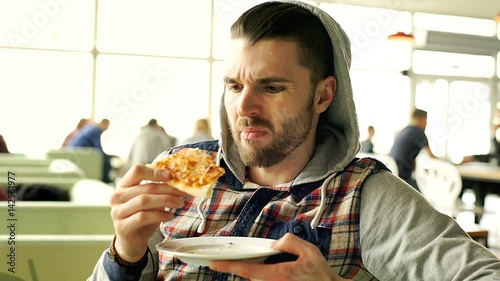 Man in hood looks dissatisfied while eating tasteless pizza, steadycam shot
