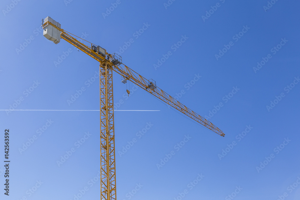 high crane on clear blue sky with a passing aircraft