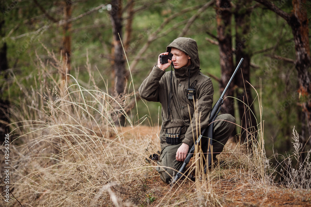 male hunter with binoculars ready to hunt, holding gun and walking in forest.