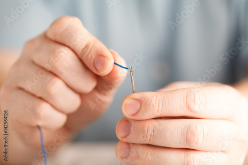 Thread into the needle. Close-up of man pulling thread into the needle