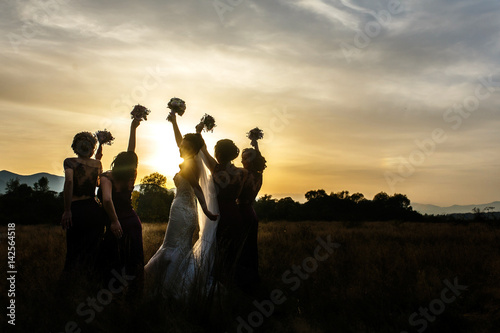 Bride and bridesmaids look over their shoulders posing on the field