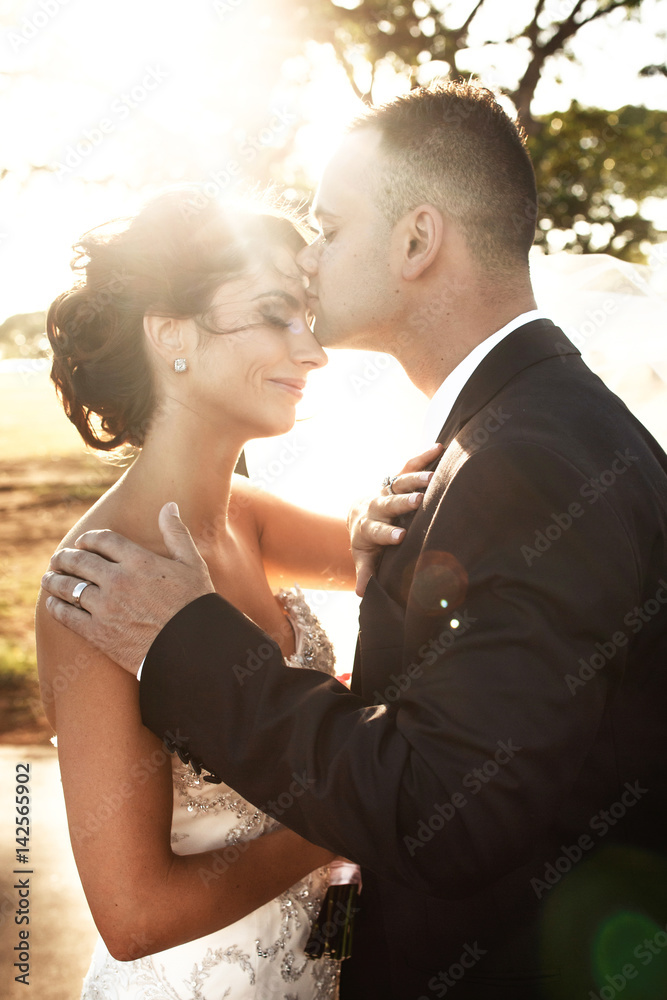 Summer sun shines over groom kissing bride's head Summer sun shines over groom kissing bride's head