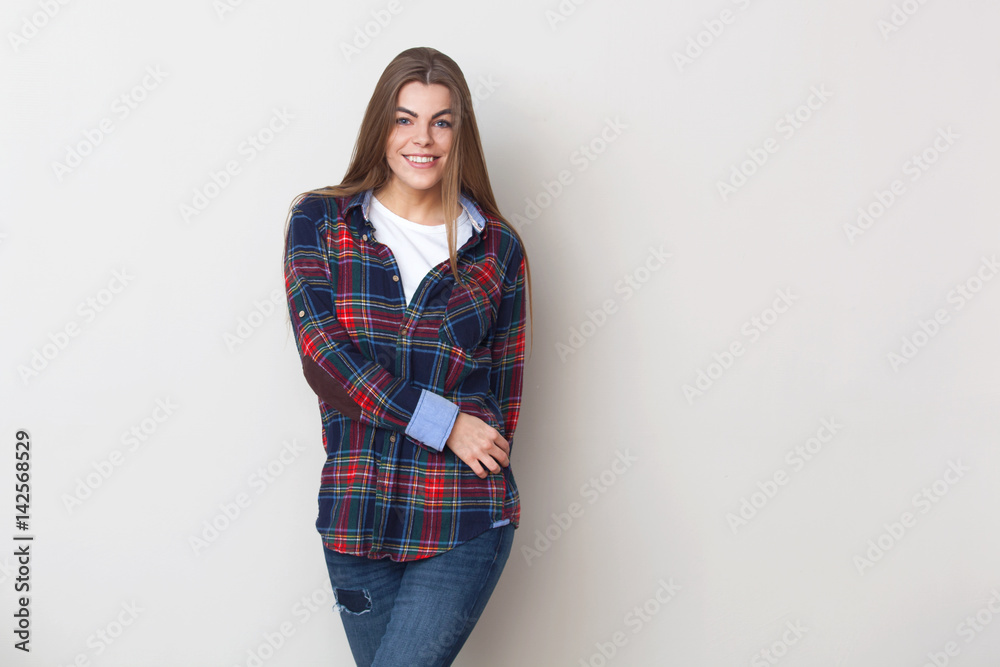 Happy young woman in plaid shirt posing against wall. Happy young woman in plaid shirt posing against wall.