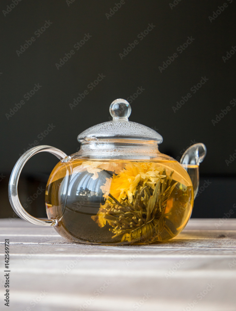 a glass tea pot with Flower Chinese tea on wooden table in front of dark background a glass tea pot with Flower Chinese tea on wooden table in front of dark background