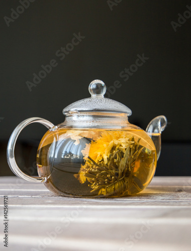 a glass tea pot with Flower Chinese tea on wooden table in front of dark background