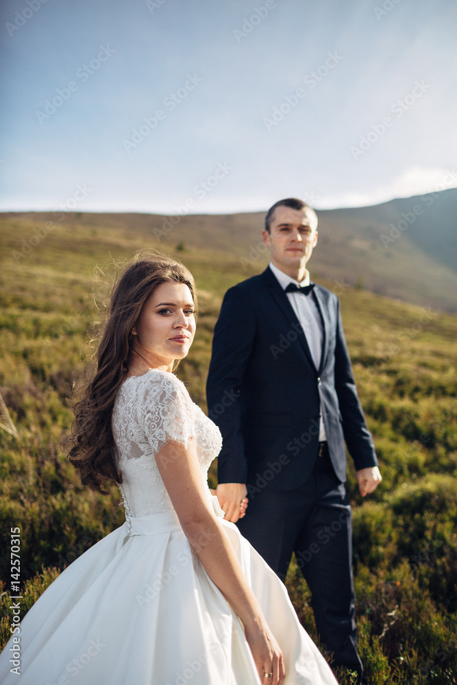 Look from behind at bride and groom standing on sunny hill in the morning