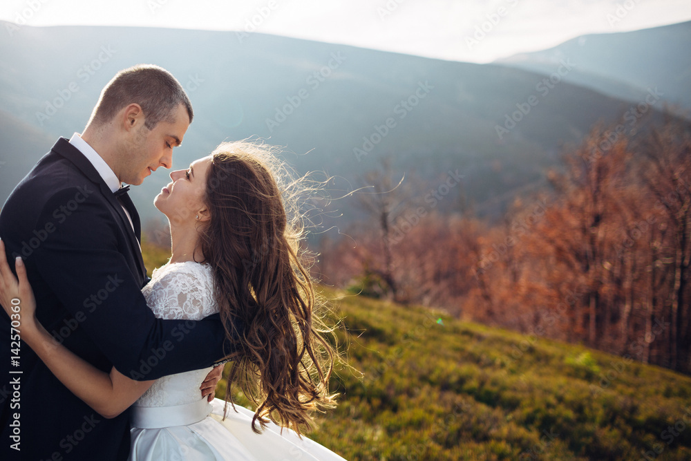Tender hugs of lovely wedding couple standing on the spring hill